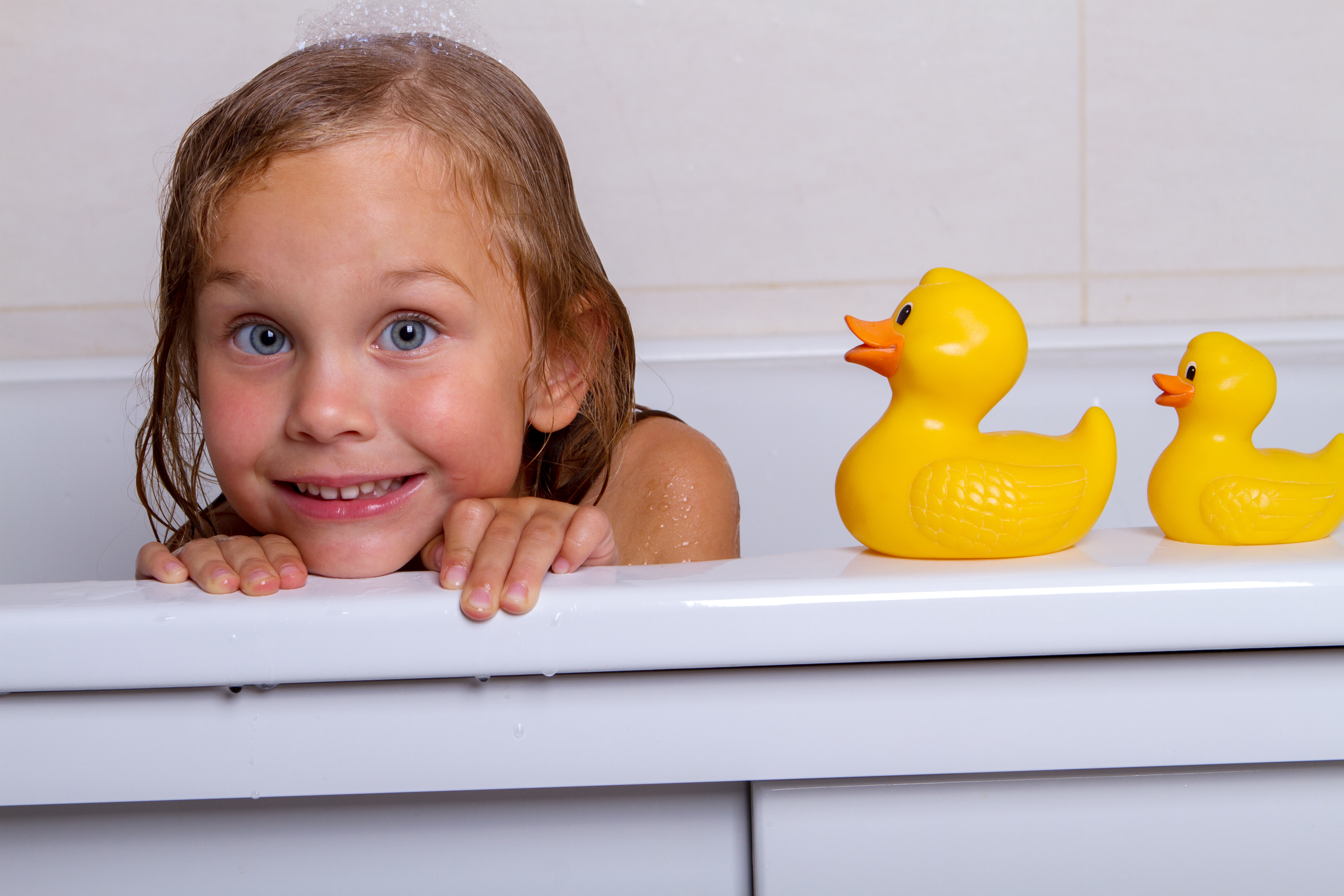 bath time fun with smiling little girl in tub with three yellow rubber ducks
